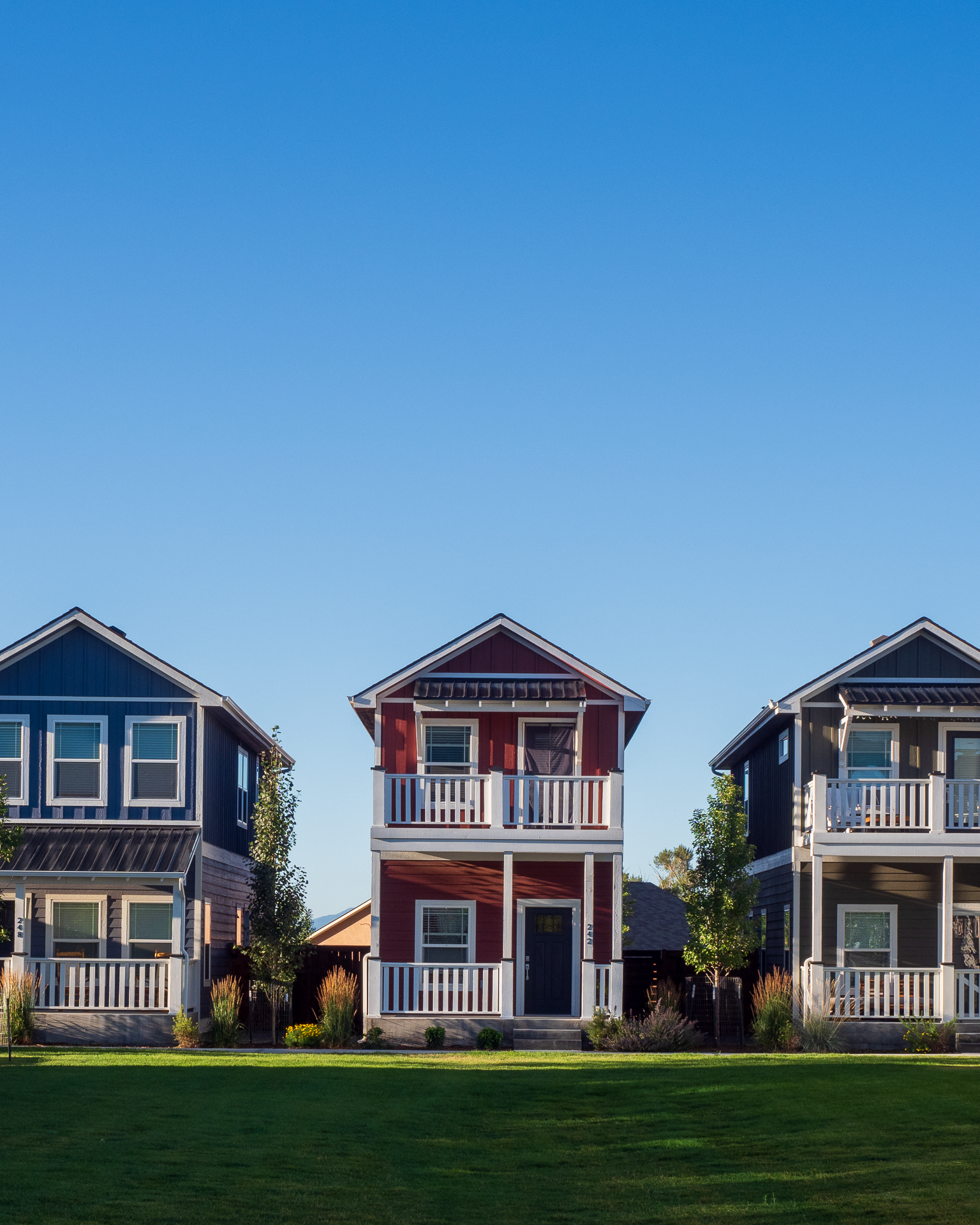 Colorful row of modern modular houses by Fading West with balconies and gabled roofs on a bright, clear day.
