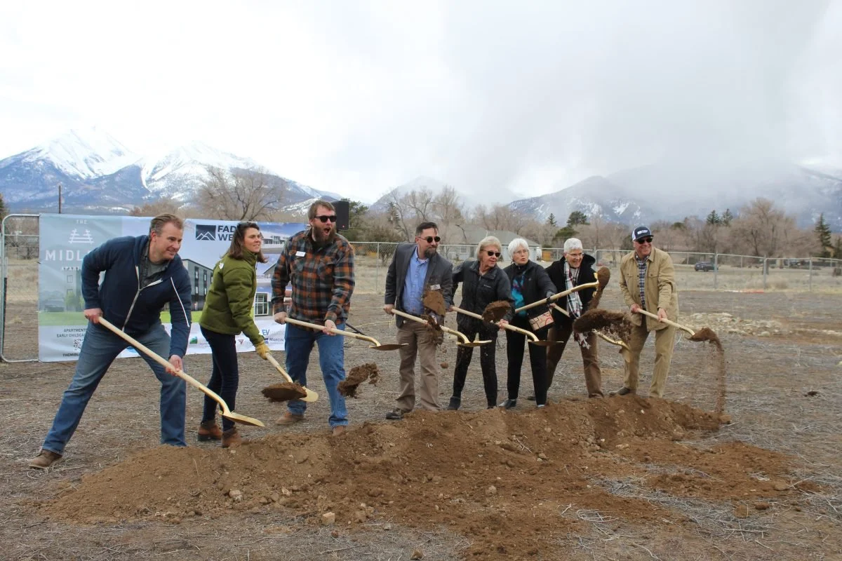 Group of people participating in a  Fading West groundbreaking workforce housing project ceremony, digging into the dirt with shovels, with mountains in the background.