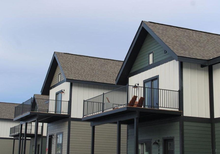 Side view of Fading West modern modular townhouses with balconies, gabled roofs, and a cloudy sky in the background.