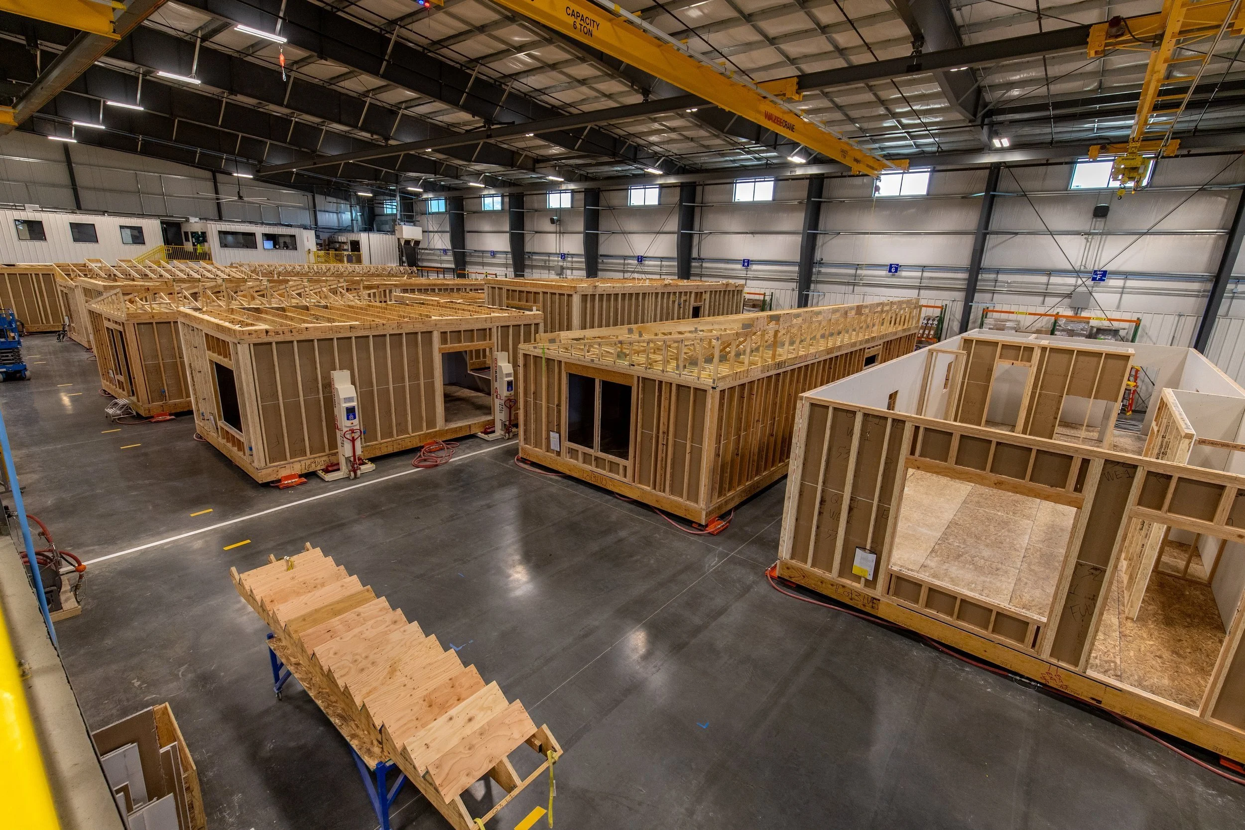 Interior of the Fading West Modular Factory warehouse with wooden framework for building structures, a staircase, and overhead crane system.