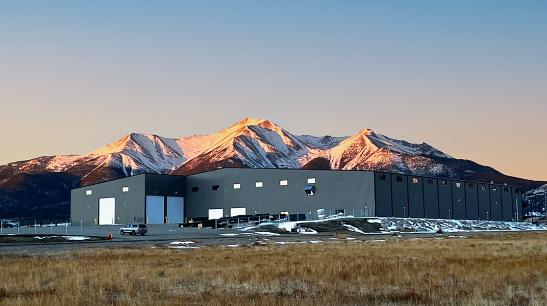 Image of the Fading West industrial warehouse building in Buena Vista, CO with snow patches on the ground, mountains in the background at sunset.