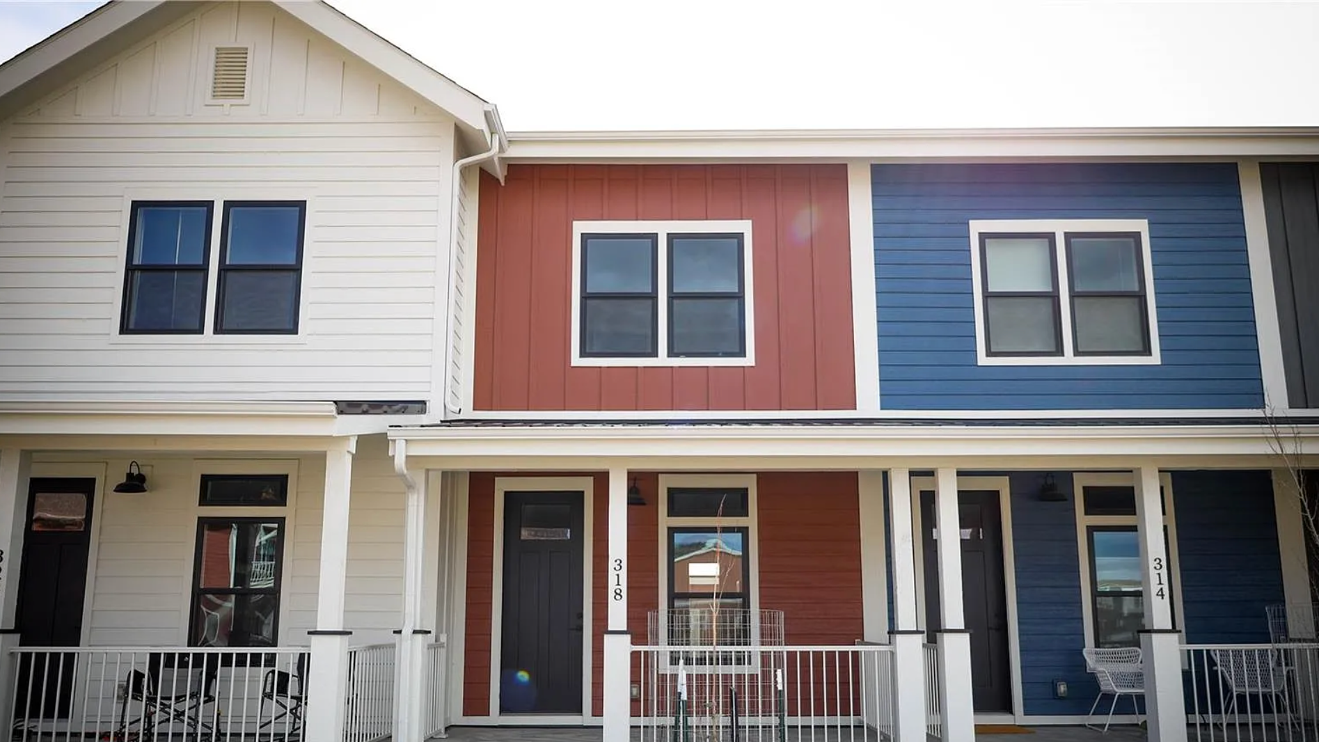 A row of colorful two-story modular townhouses with white trim, featuring a combination of cream, red, and blue siding, with black windows and doors.