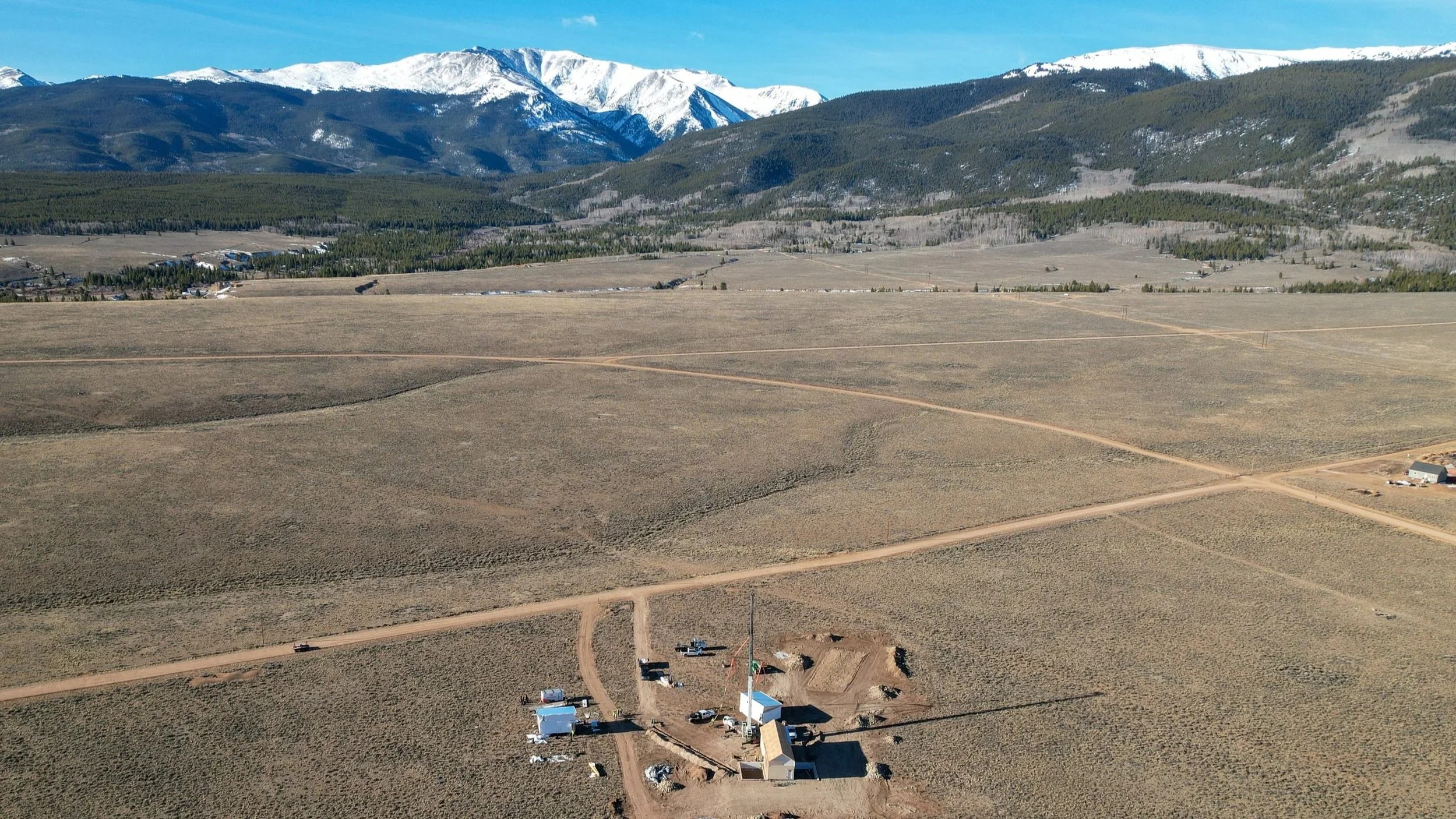 A wide landscape view of a mountainous area with snow-capped peaks in the background, a large open field in the foreground. Single Family modular home installation in Colorado.