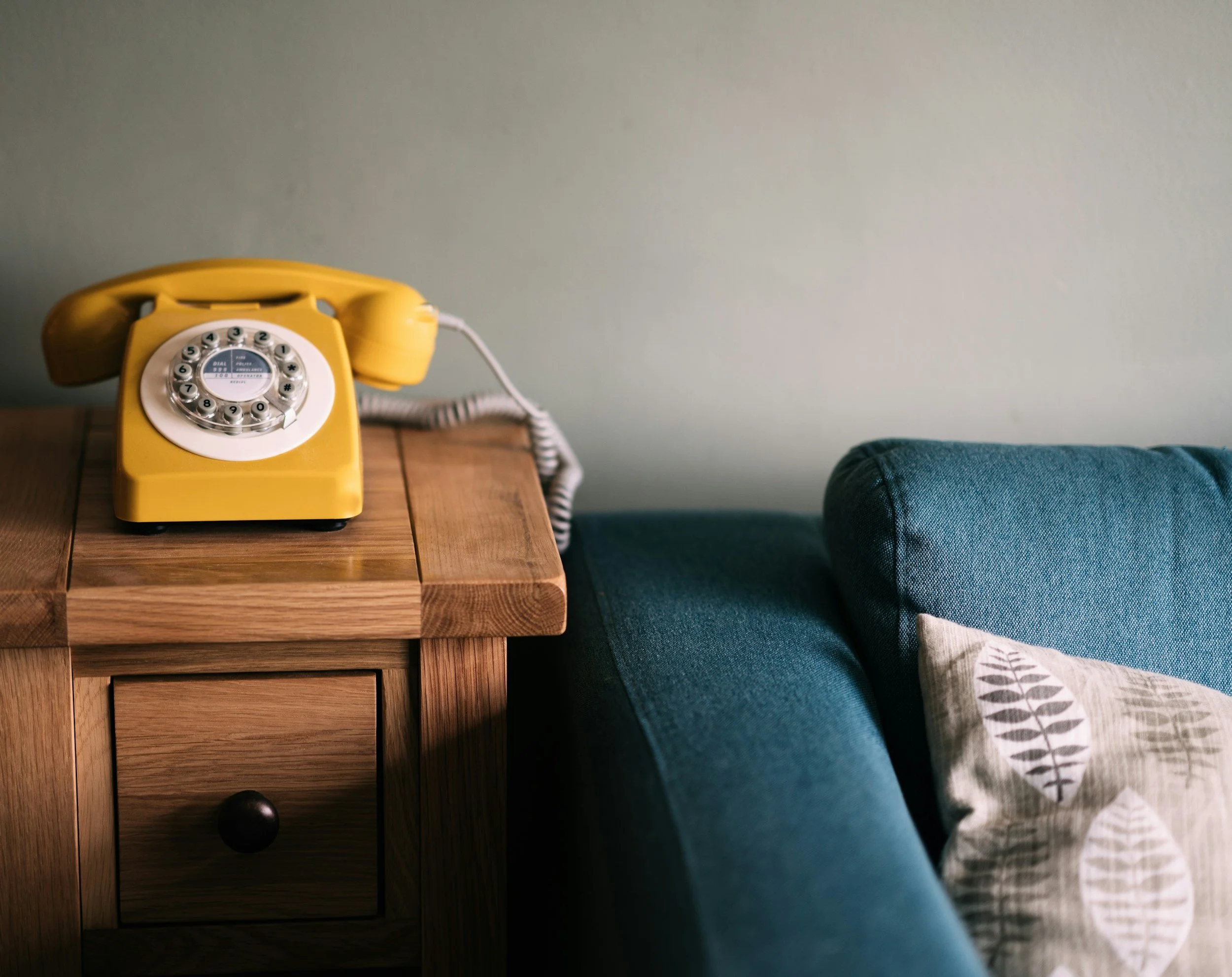 Yellow rotary phone beside a chair.