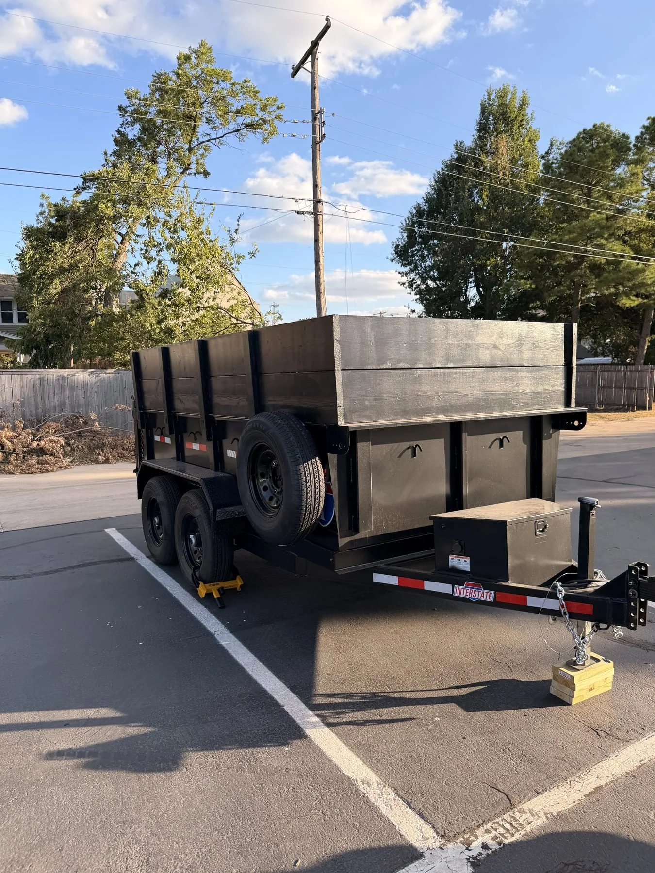 Rear view of the Nicks Junk Removal black dump trailer with tall wooden sides, tandem axles and a spare tire