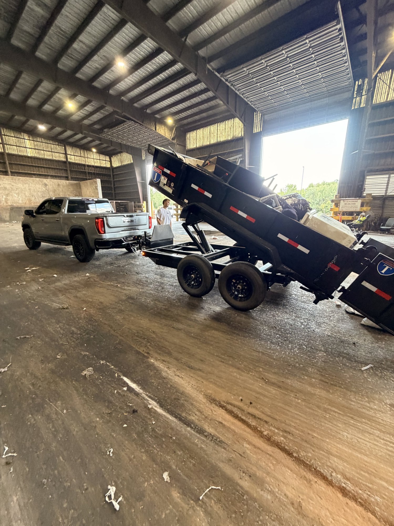 Nicks Junk Removal dump trailer tipped up, unloading at a covered disposal facility with the silver pickup in the background