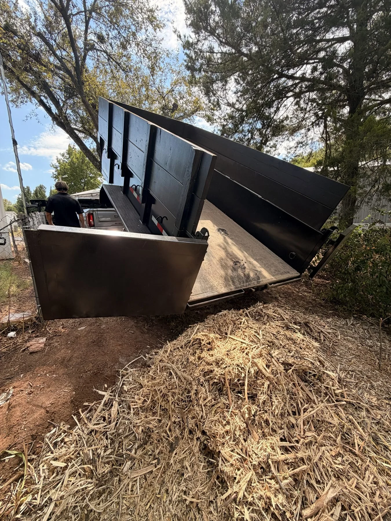 Nicks Junk Removal dump trailer tilted up, unloading a pile of wood chips and brush at a disposal site