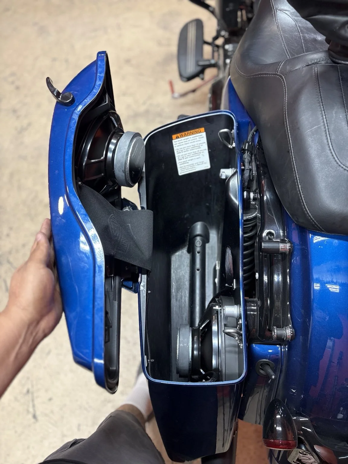 A person holding a blue motorcycle fairing, showing the internal components and a warning label inside the fairing.