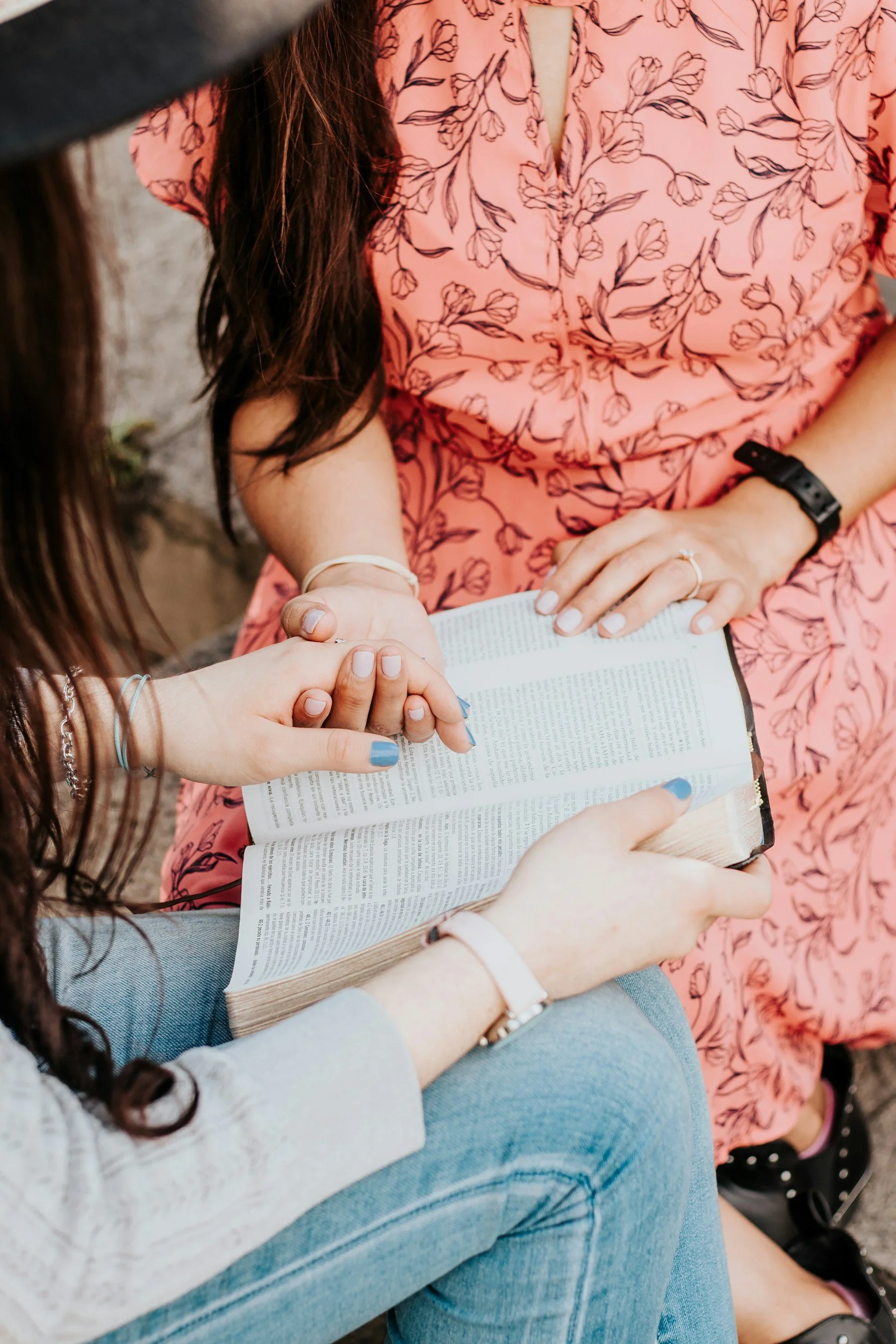Close-up of two people holding hands and reading a book together.