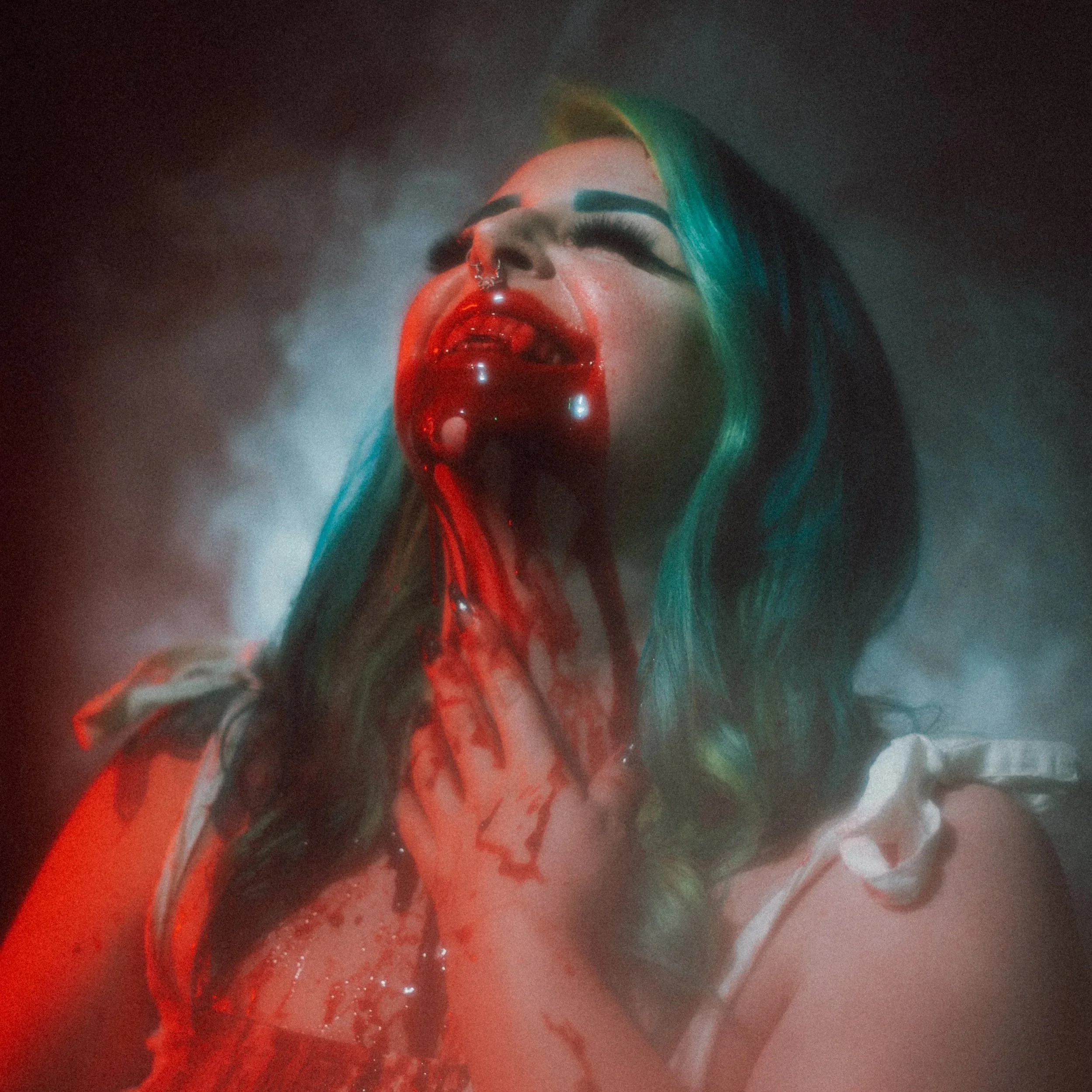A person with teal hair, red lipstick, and a septum piercing winks with lips parted, looking at the camera, with red liquid dripping from the mouth and chin.