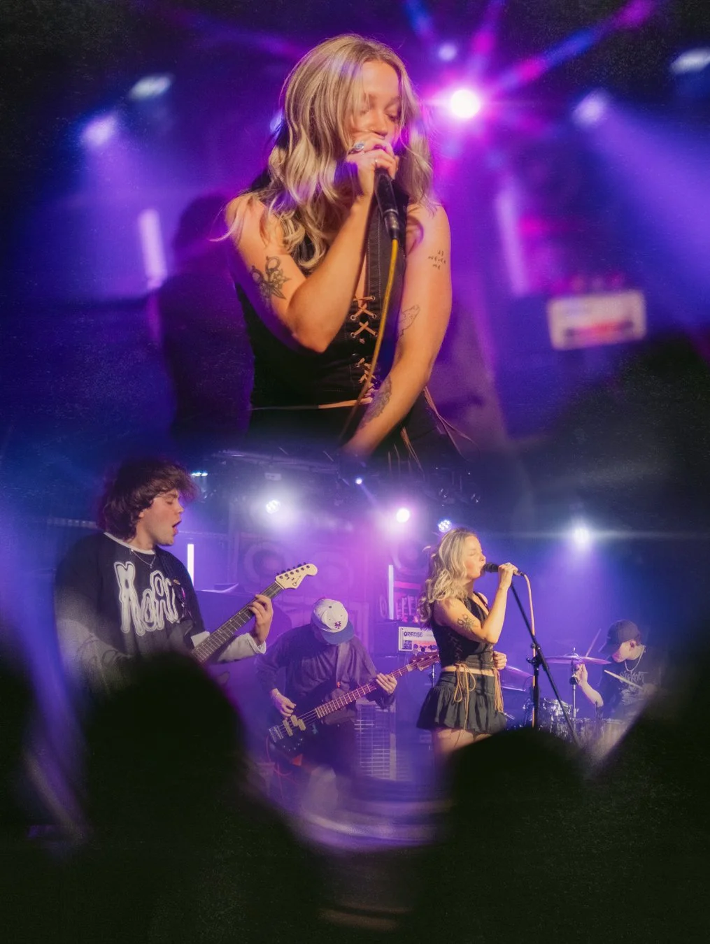 A female singer with tattoos on her arms performing on stage with a band, illuminated by purple stage lights.