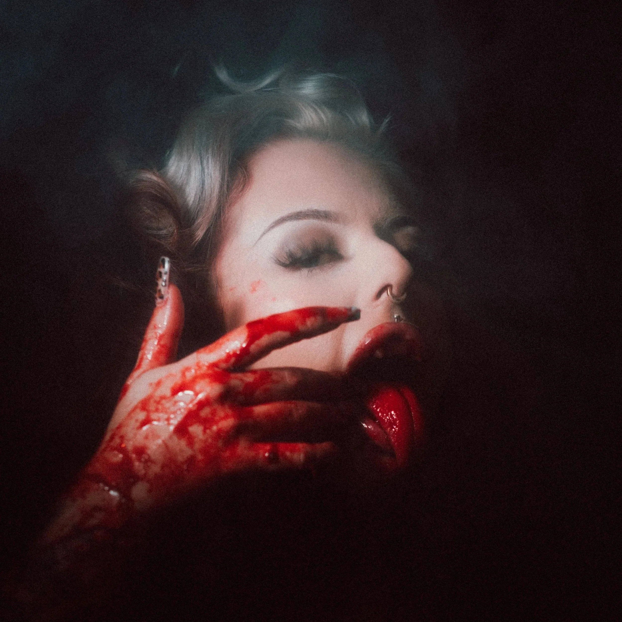 Partial view of a woman's face with makeup, curly hair, and earrings, partially covered by bloodied fingers on her face.