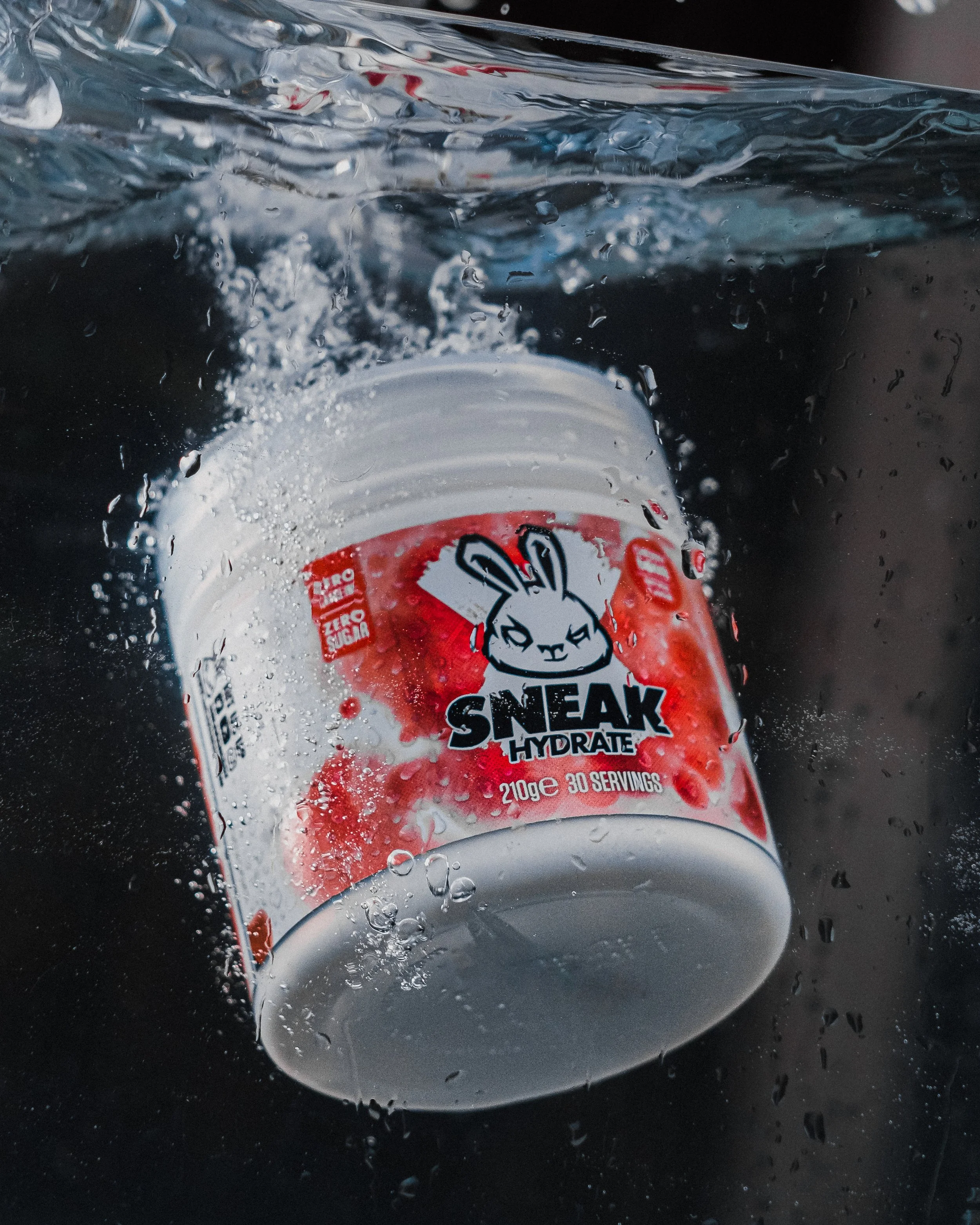 A plastic bottle of Sneak Hydrate sports drink being submerged in water, with water splashing around.
