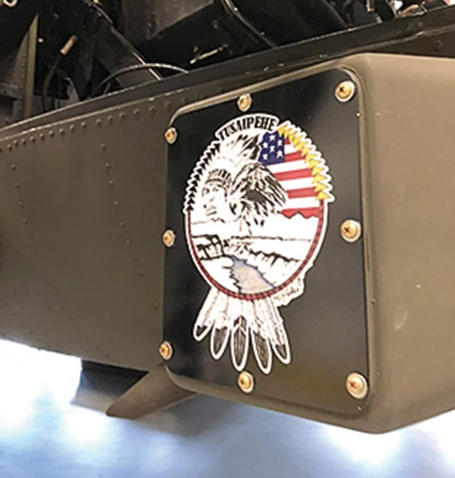 Close-up of an insignia with a feathered headdress, American flag, and landscape, attached to a military aircraft fuselage.