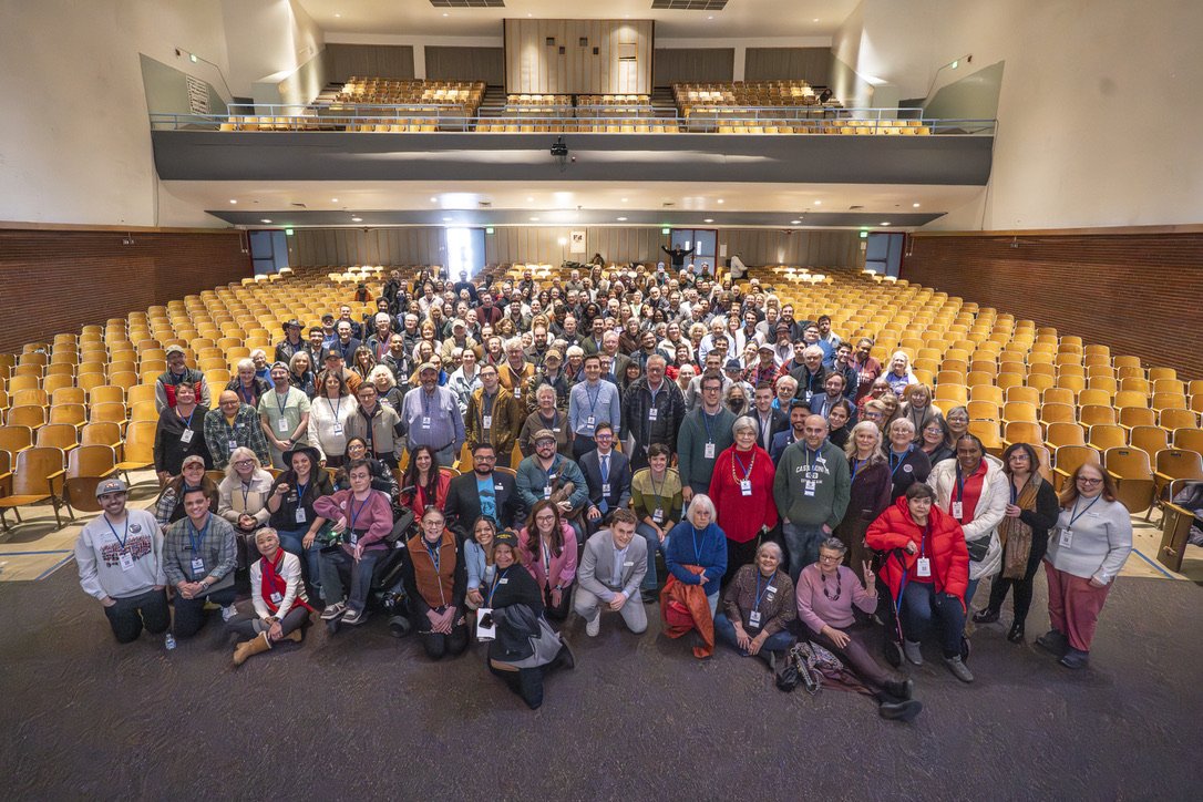 Large group of people gathered in an auditorium or conference hall, posed for a group photo.