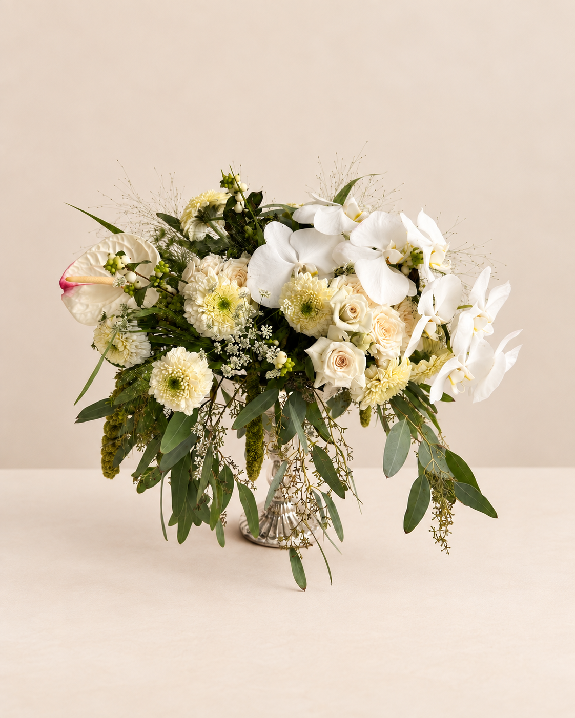 White and green floral arrangement by Grove Floral Studios in Miami, featuring orchids, roses, gerberas, airy textures, and seasonal greenery in an elegant silver pedestal vase.