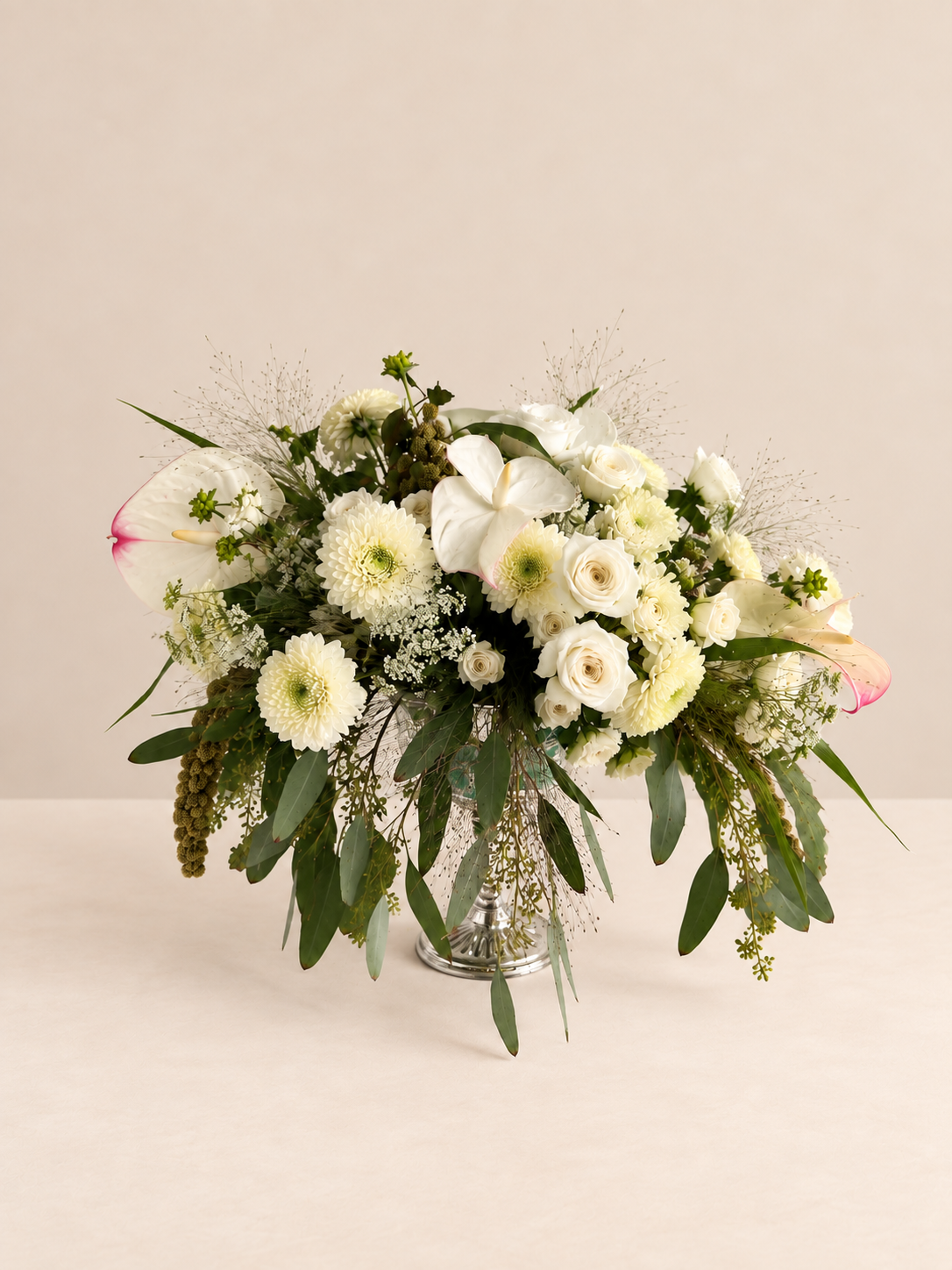 White and green floral arrangement by Grove Floral Studios in Miami, featuring orchids, roses, gerberas, airy textures, and seasonal greenery in an elegant silver pedestal vase.