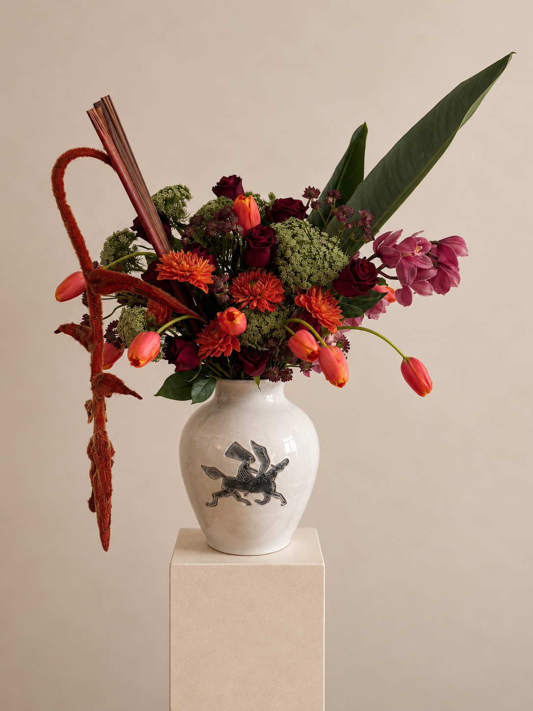 Sculptural floral arrangement by Grove Floral Studios in Miami, featuring orange tulips, burgundy roses, orchids, textural greenery, and architectural foliage arranged in the Pegasus Vase.