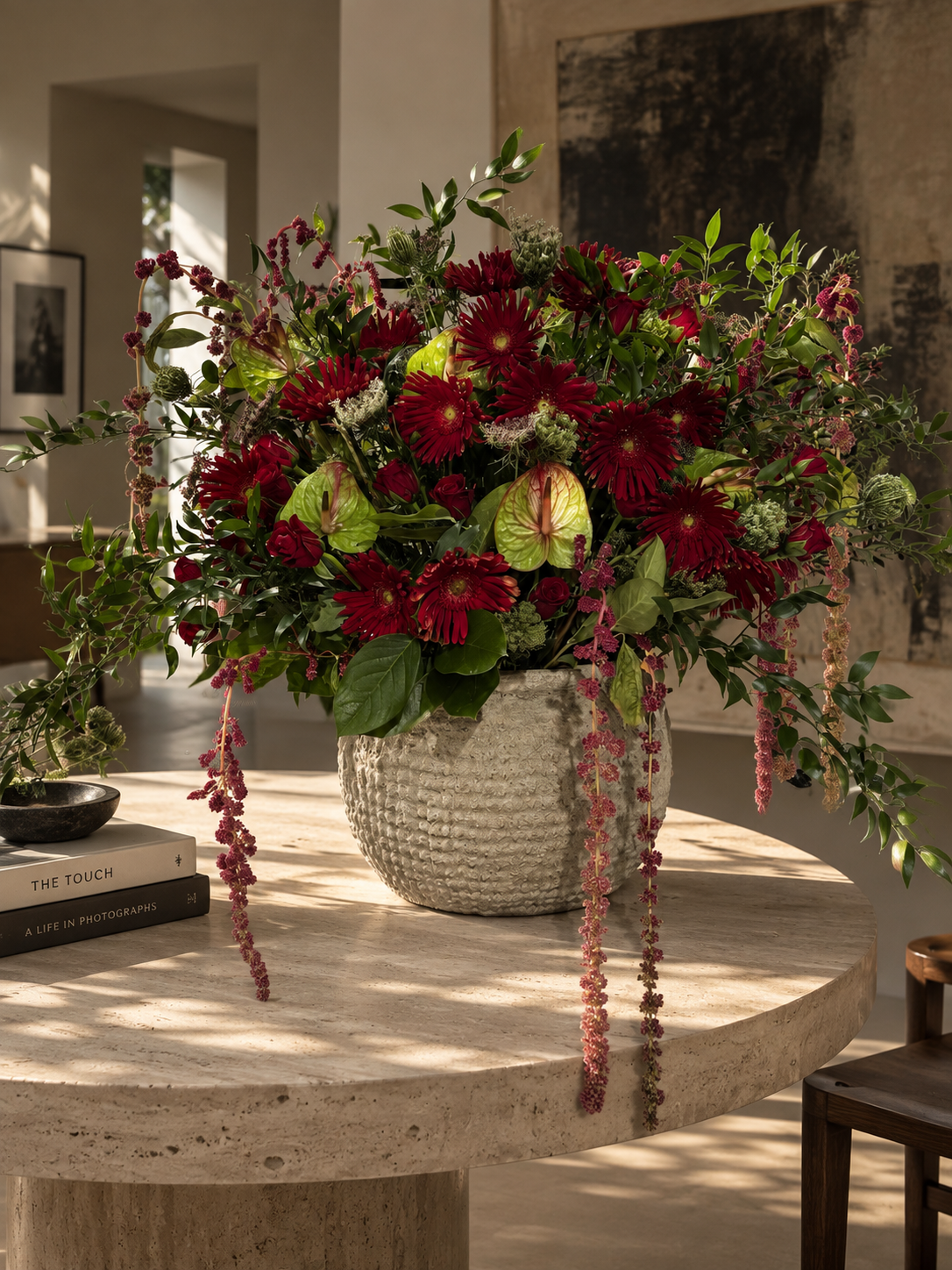 Large sculptural red and green floral arrangement by Grove Floral Studios in Miami, featuring deep red gerbera daisies, green anthuriums, roses, cascading amaranthus, and textural greenery in a statement ceramic vessel.