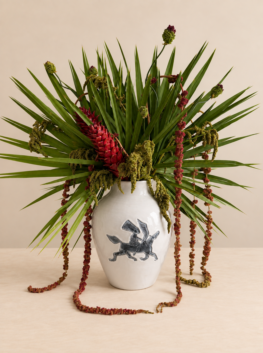 Sculptural tropical floral arrangement by Grove Floral Studios in Miami, featuring spiked green foliage, red tropical blooms, cascading textural amaranthus, and botanical accents arranged in the Pegasus Vase.