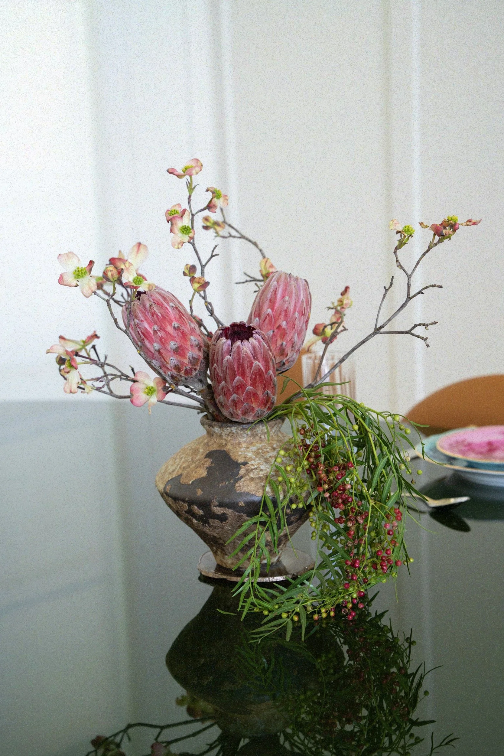 Small modern arrangement with pink proteas, dogwood & pepper berries in a brutalist vase.