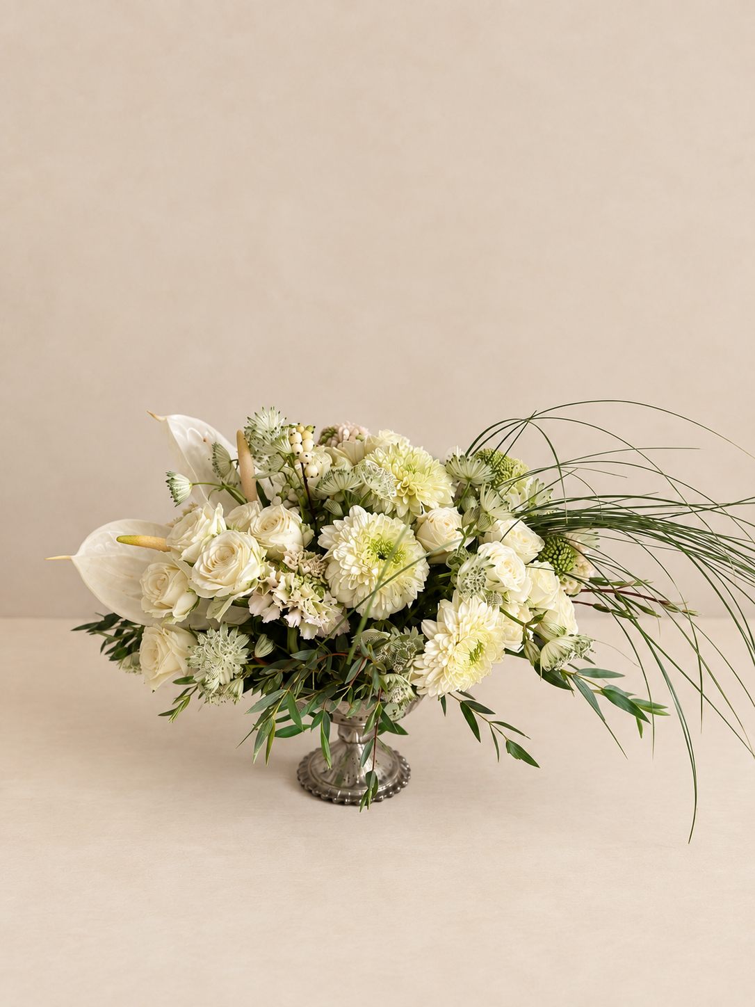 White and green floral arrangement by Grove Floral Studios in Miami, featuring orchids, roses, gerberas, airy textures, and seasonal greenery in an elegant silver pedestal vase.