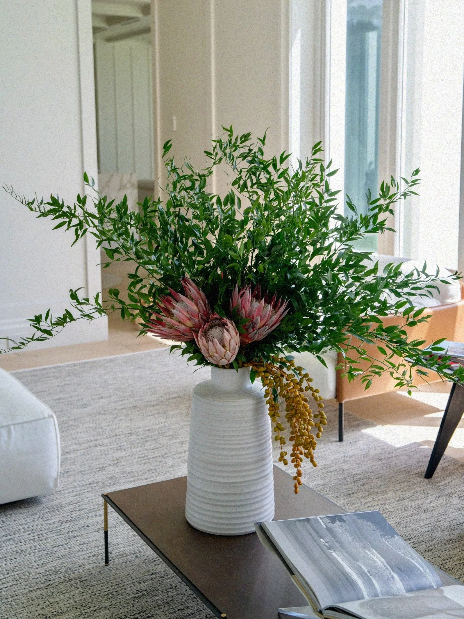 Large Modern arrangement with King Proteas, Italian Ruscus & dates in a white vase.