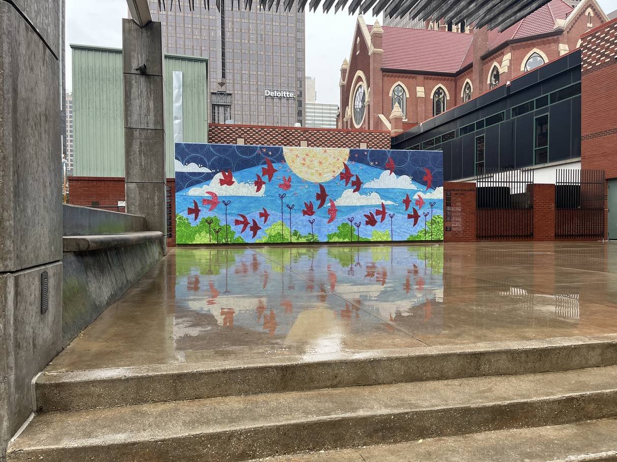 The completed Looking Up mural installed in downtown Dallas after rain, reflected in the wet plaza pavement.