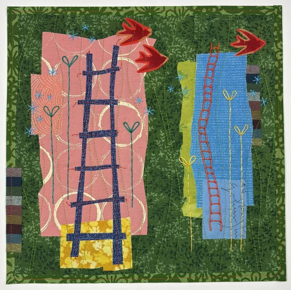A colorful quilt featuring two textile panels with embroidered designs of ladders, hearts, and flowers, set against a green leafy background with red floral appliqués in the top right corner.