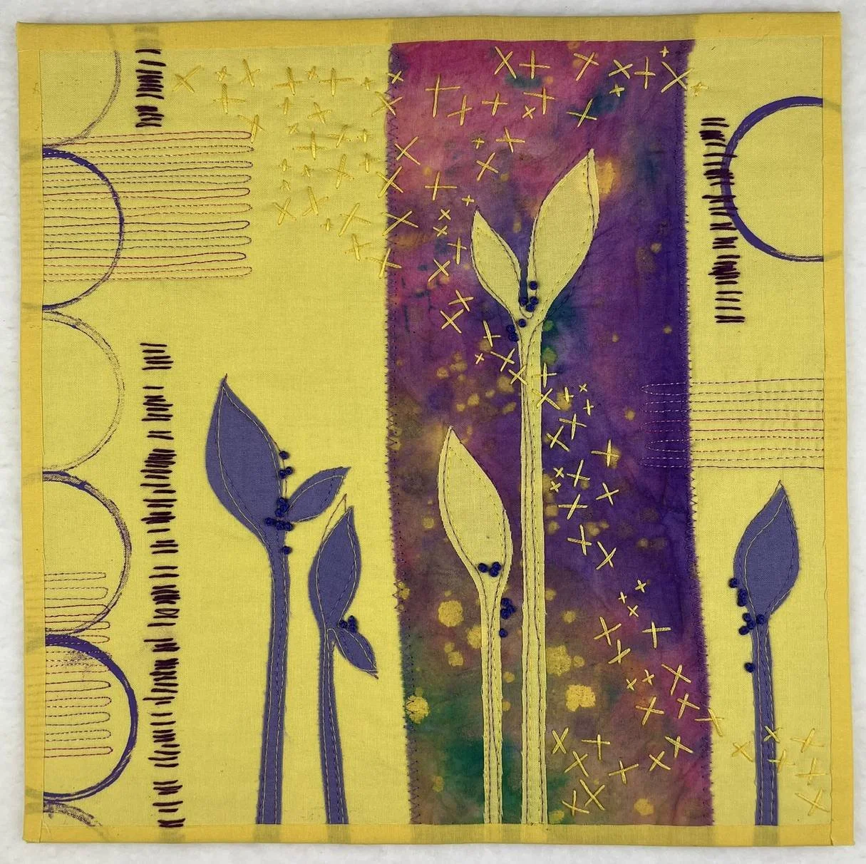 Culmination, an art quilt by Deborah Boschert featuring blue-grey appliquéd leaves and golden cross-stitched seeds on yellow and purple fabric.