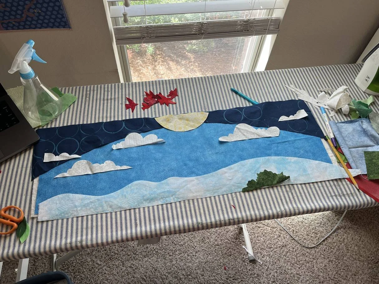 The Looking Up mural design in progress, with fabric pieces laid out on a striped work table.