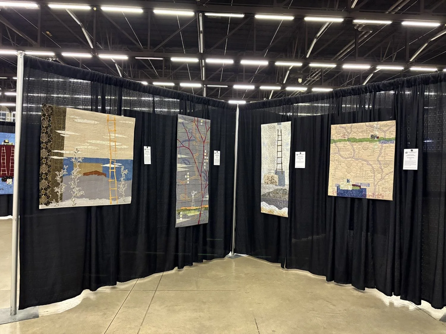 Four of Deborah Boschert's art quilts in neutral cream, tan, and grey tones displayed at the Dallas Quilt Show.