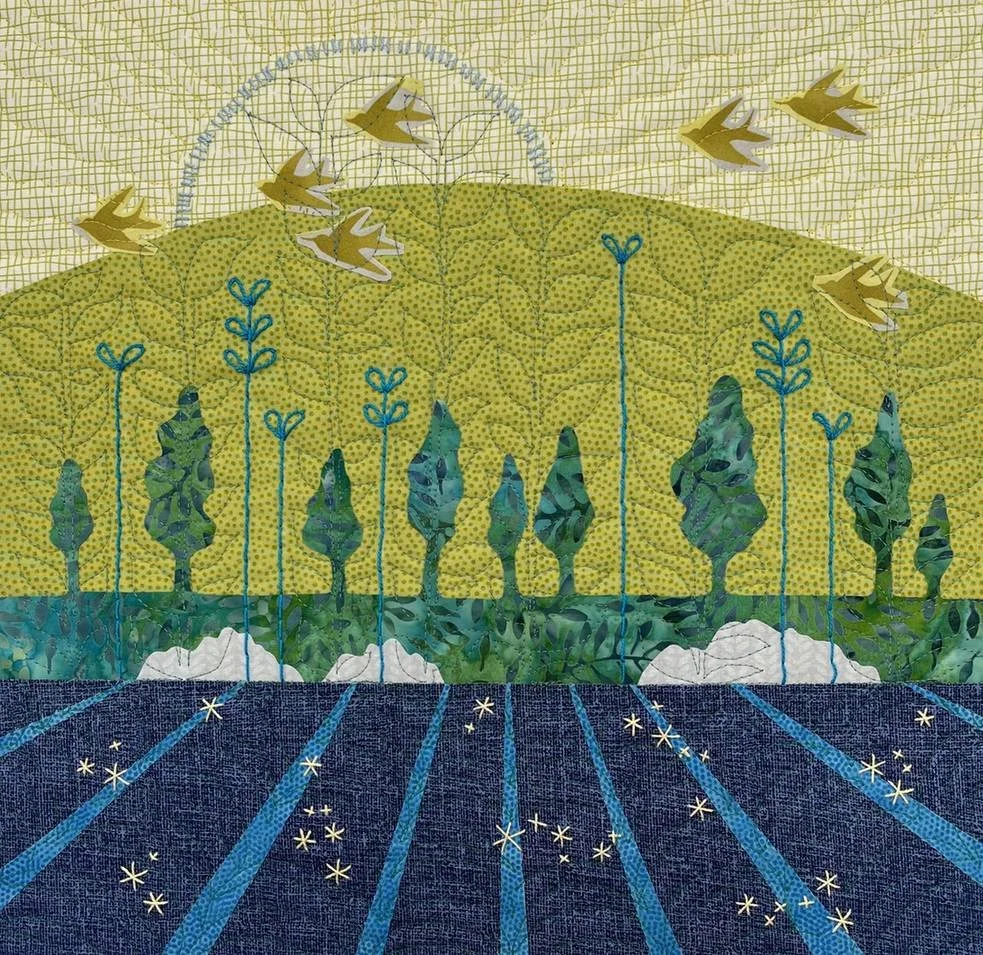 A colorful quilt featuring a landscape scene with trees, a hill, and birds flying in the sky, with stars on the ground.