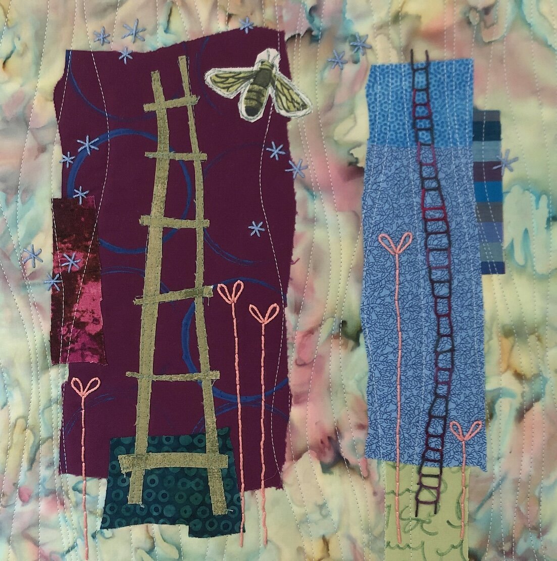 A quilt with embroidered designs of murals, insects, and flowers, including a large bee and a dove, set against a multicolored, tie-dye fabric background.