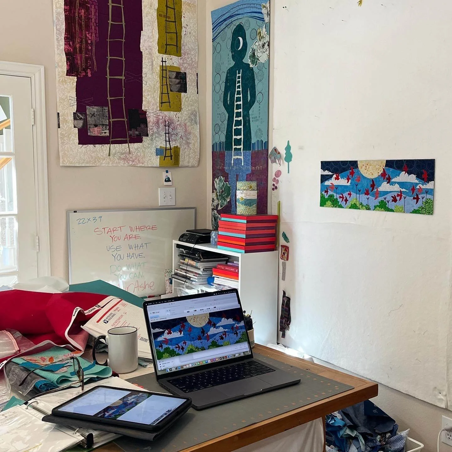Deborah Boschert's home studio with the Looking Up mural design displayed on a laptop and tablet alongside earlier figural art quilts.