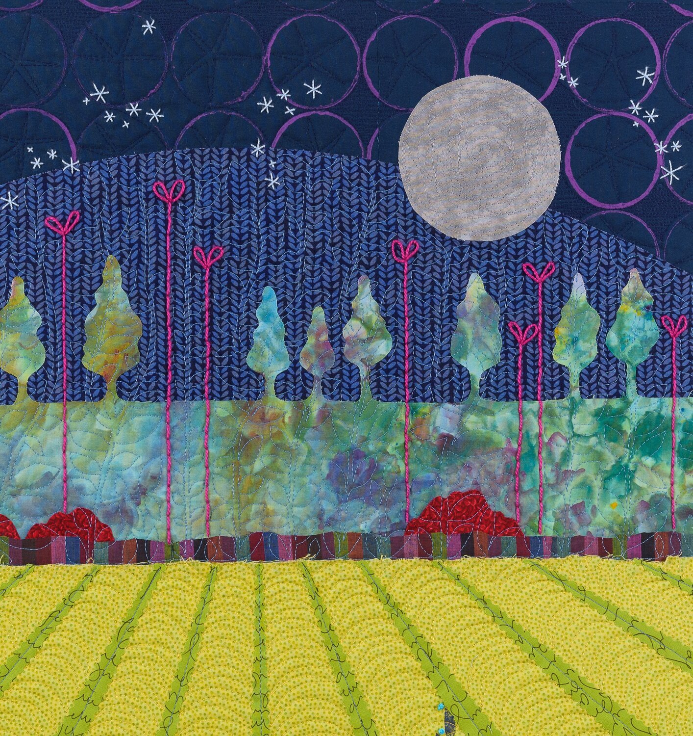 A colorful quilt depicting a landscape scene with trees, a yellow field in the foreground, a blue sky with white stars, a large full moon, and red flowers at the base of the trees.