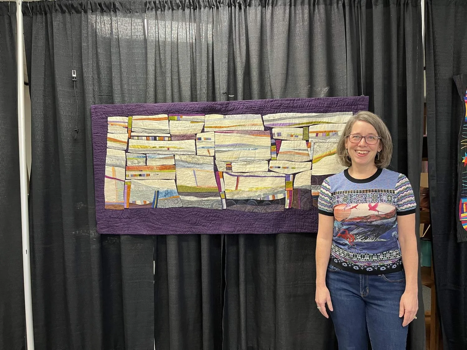 Deborah Boschert standing beside a long horizontal art quilt during her judging duties at the International Quilt Festival.