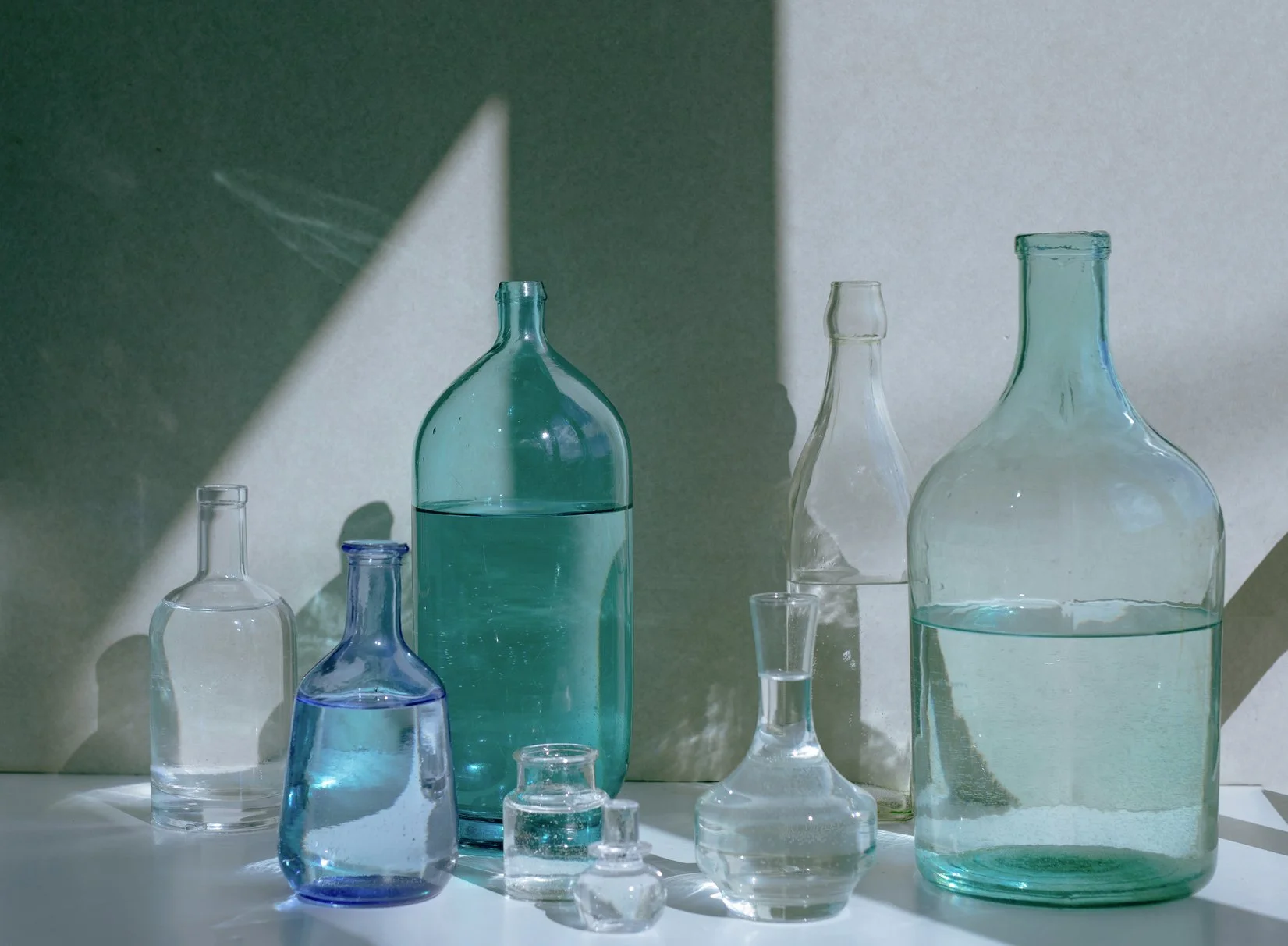A collection of translucent bottles filled with varying amounts of clear liquid. Some bottles are clear, some are aqua, and one is light blue.