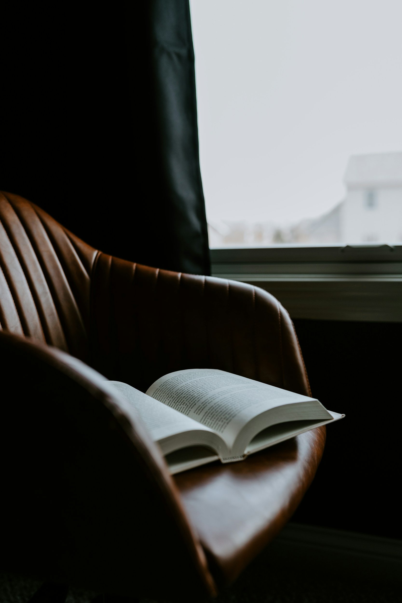 Book Edits, Proposals, Ghostwriting, Podcast and Audiobook Narration and Production. Image is of an open book resting on a brown leather chair, with a window in the background showing a rainy sky outside.