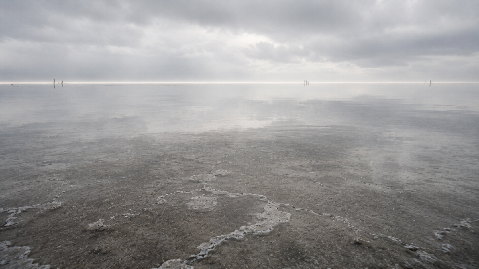 Mist drifting across a reflective mineral surface beneath a distant horizon, depicting the stable underlying substrate associated with the Kernel's continuous execution state.