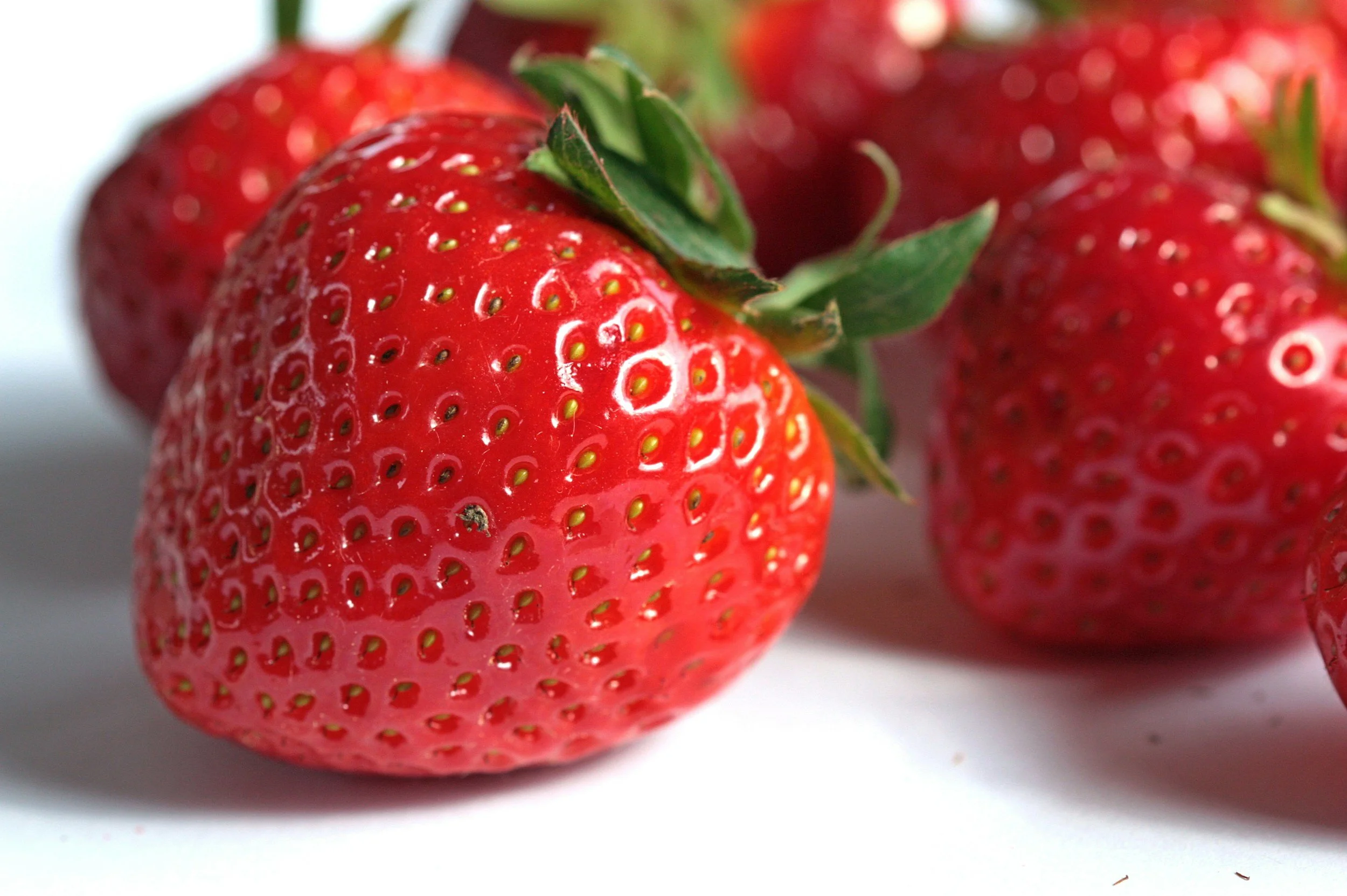 Close-up of a ripe red strawberry with green leaves, and other strawberries in the background.