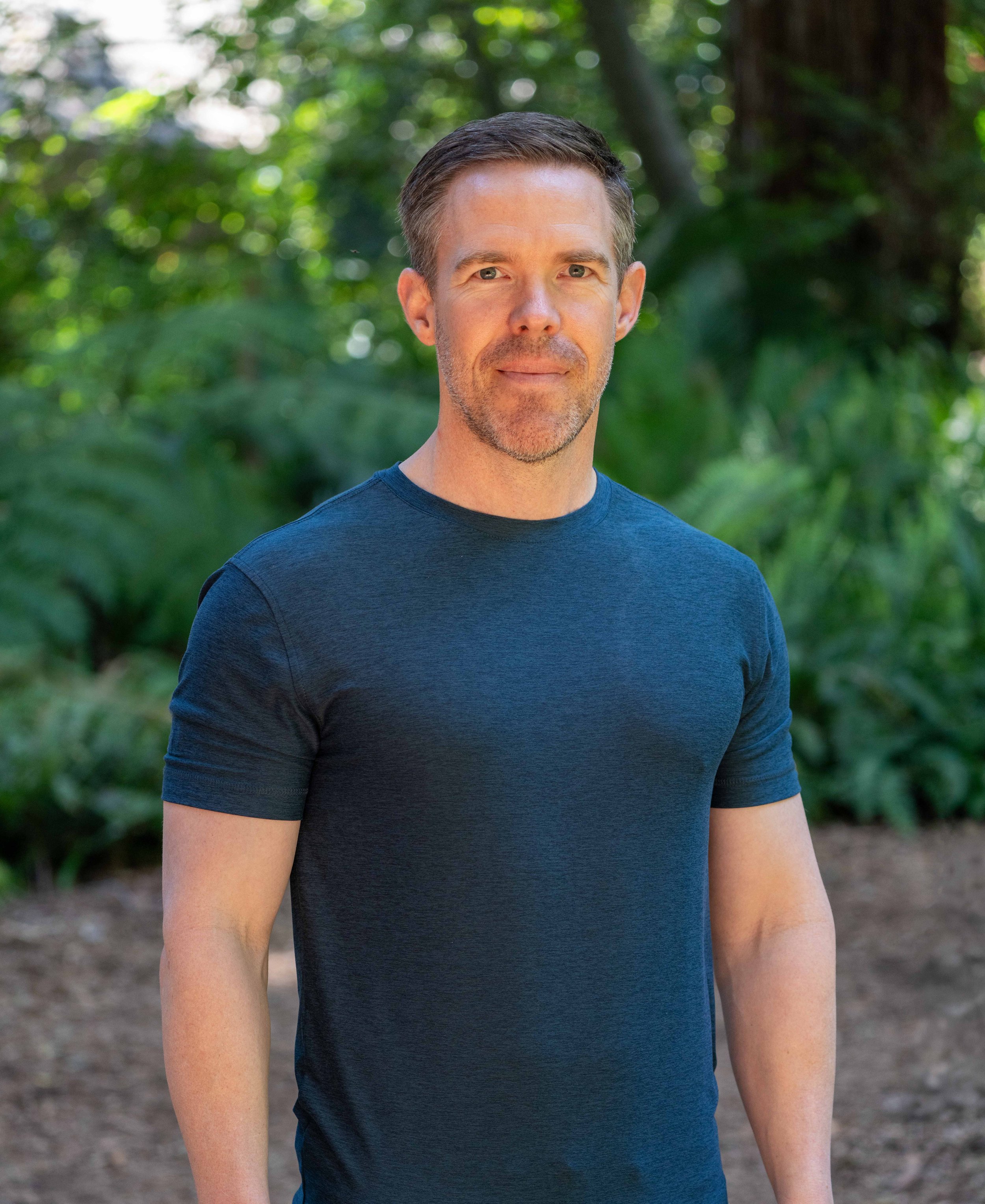 Matt Dalton, transformation coach, standing outdoors in a blue shirt with a natural green background.