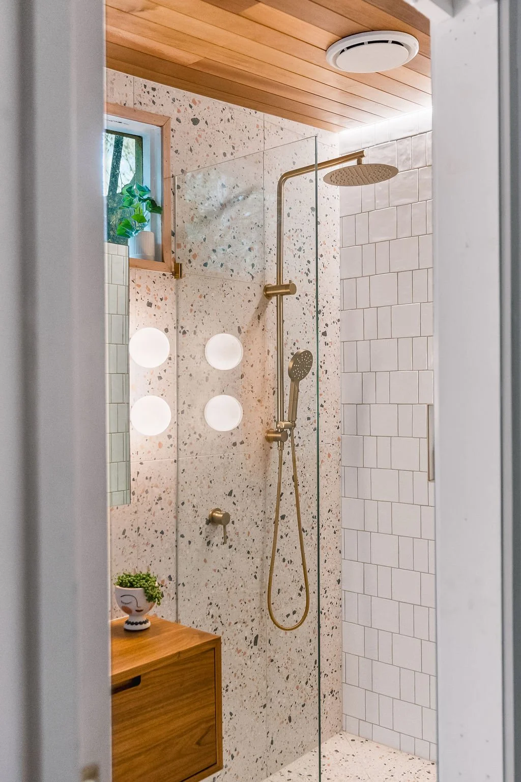 Modern walk-in shower with terrazzo walls, a large rain showerhead, a hand-held shower attachment, and a wooden ceiling.