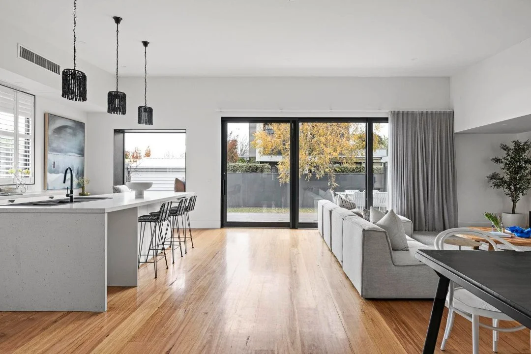 Modern open-concept living room and kitchen with hardwood floors, white walls, a white kitchen island