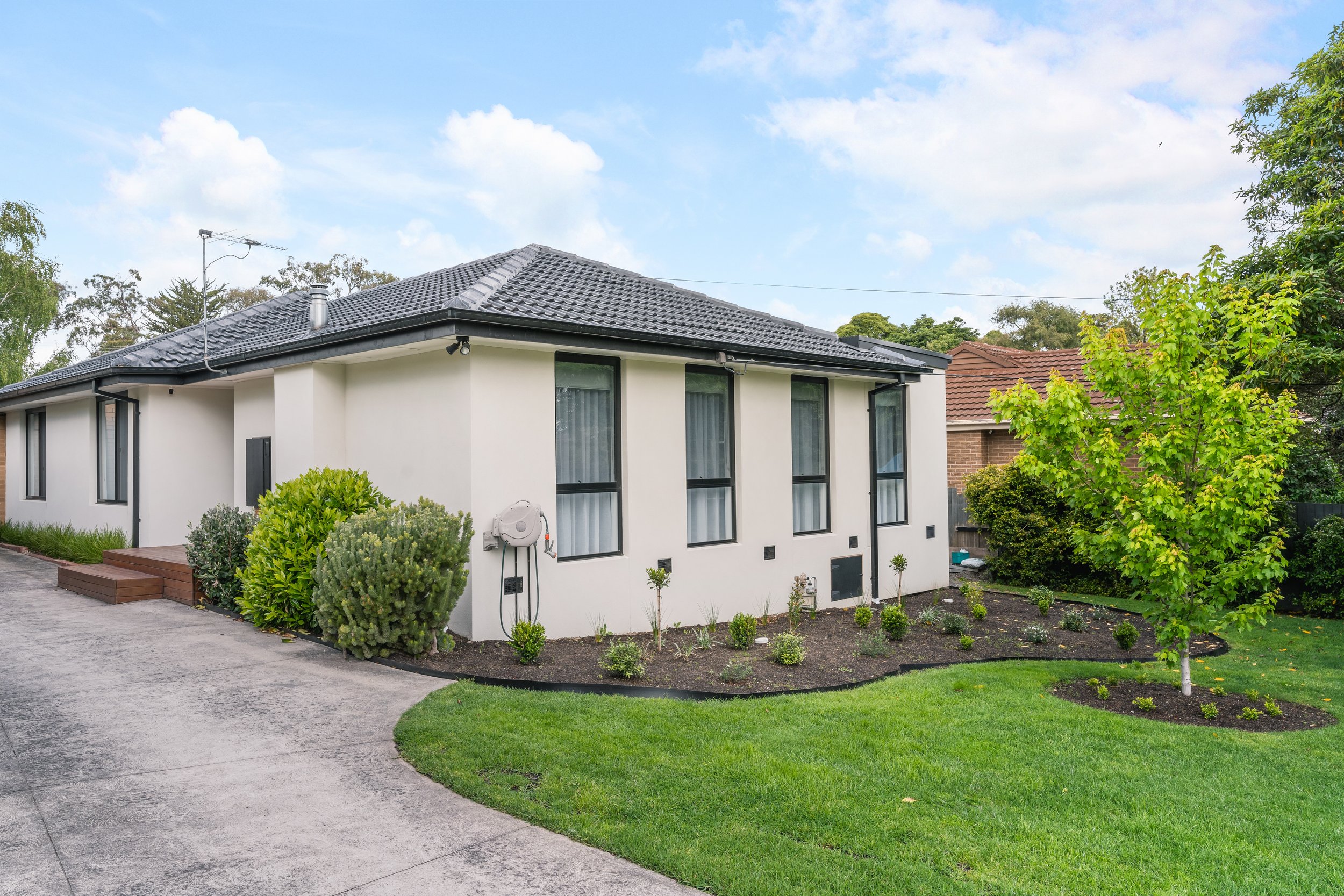 A modern white house with large windows, surrounded by a landscaped garden with bushes, small plants, and a well-maintained lawn in Yarra Valley built by Leisure Built