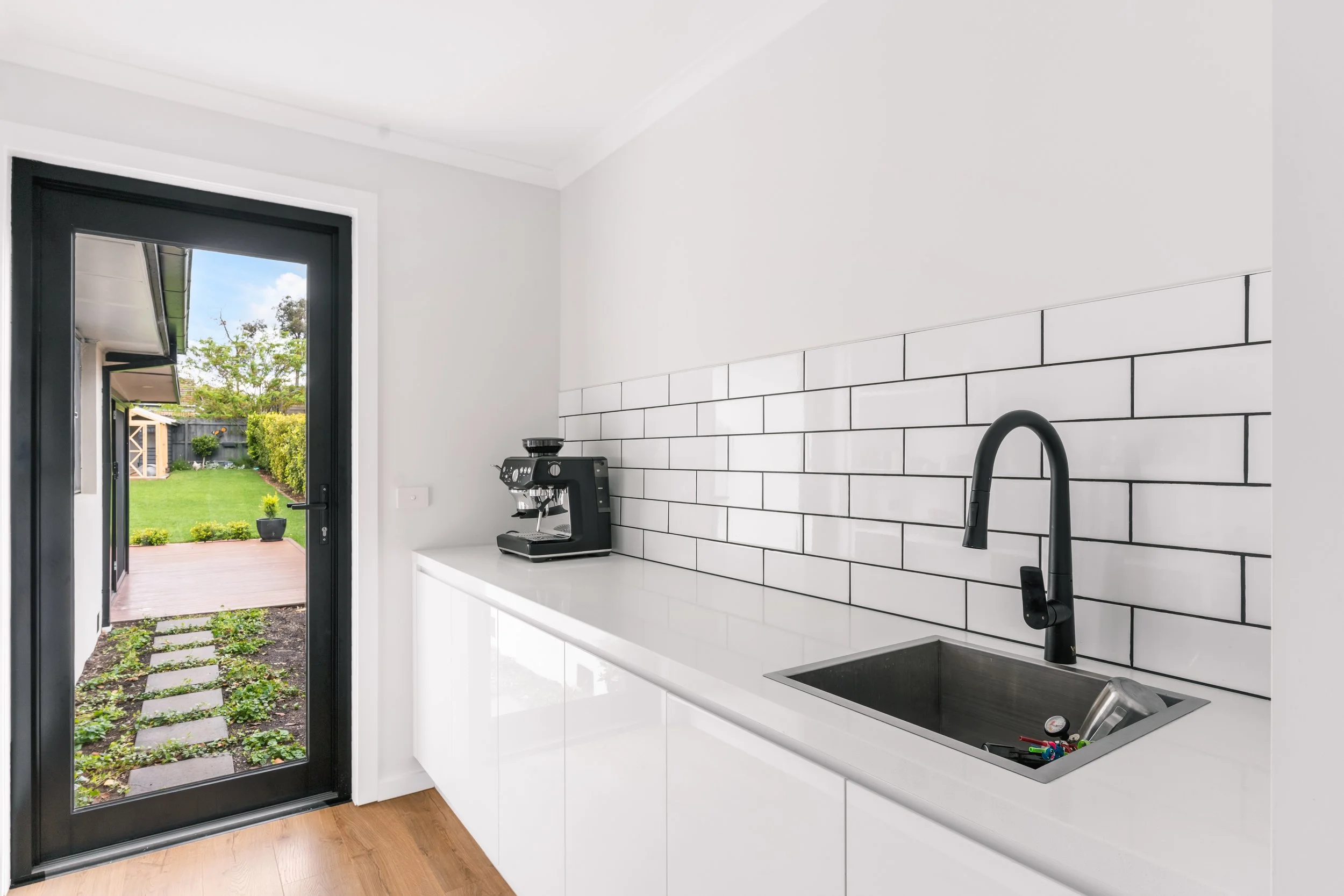 Modern kitchen with white cabinets, black sink, black faucet, white subway tile backsplash in Yarra Valley built by Leisure Built