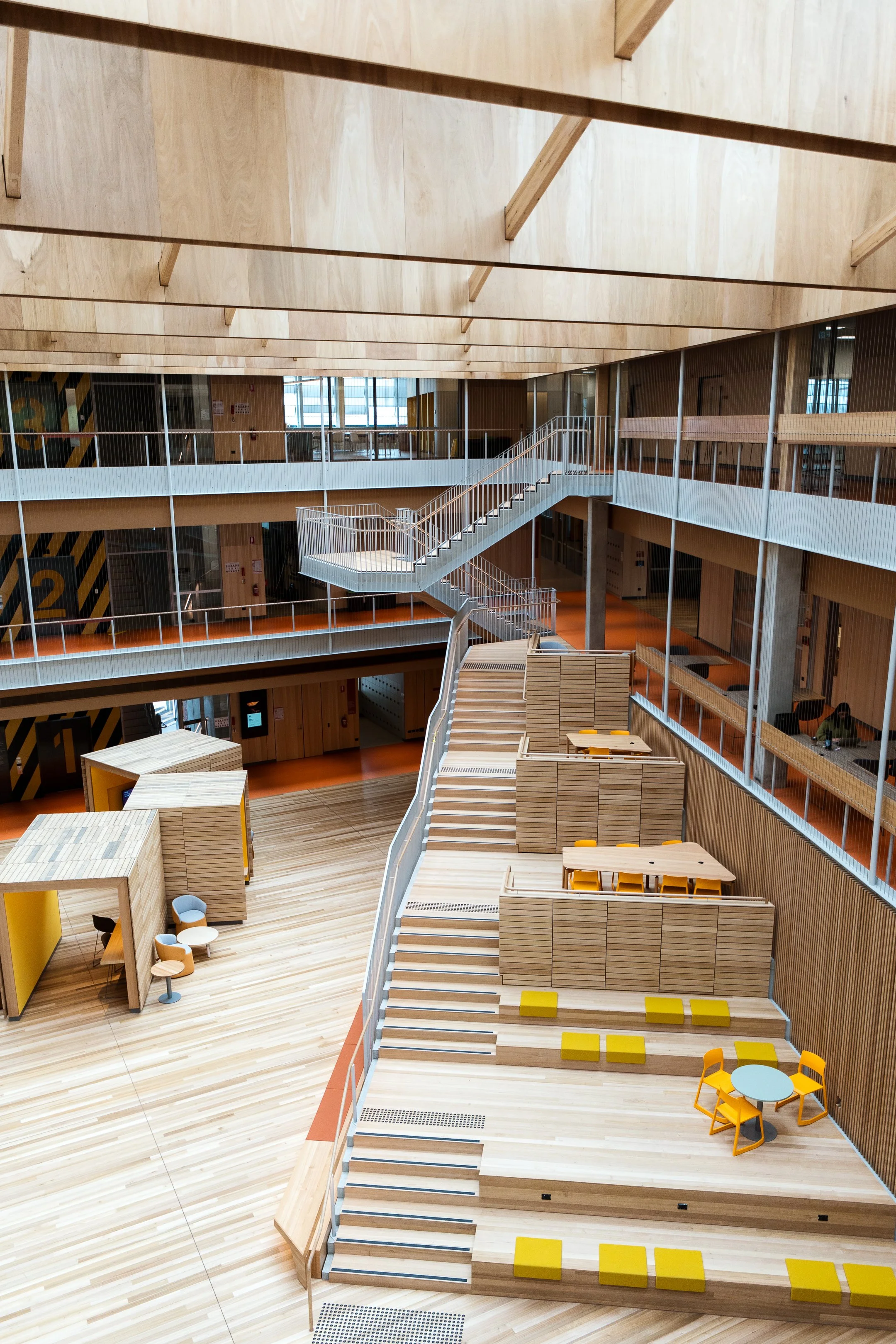 Open multi-level modern building interior with wooden floors, stairs, and open spaces for seating and socializing.