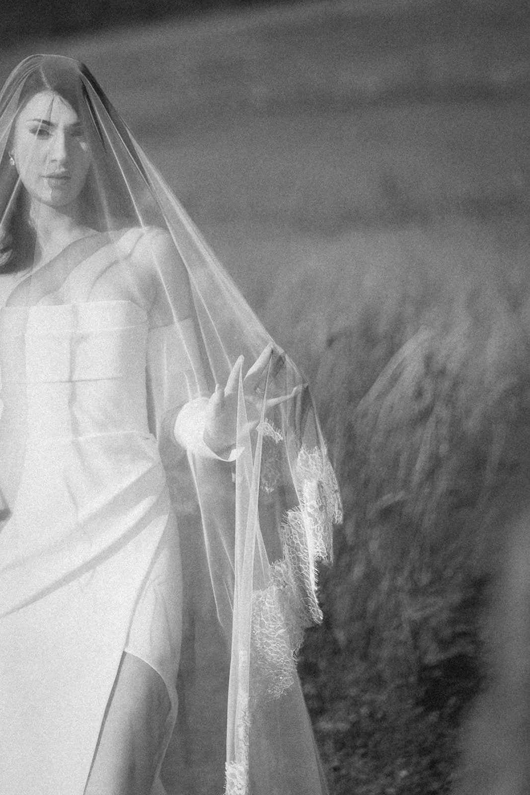 A woman wearing a wedding dress and veil outdoors, standing next to a horse and holding its bridle.