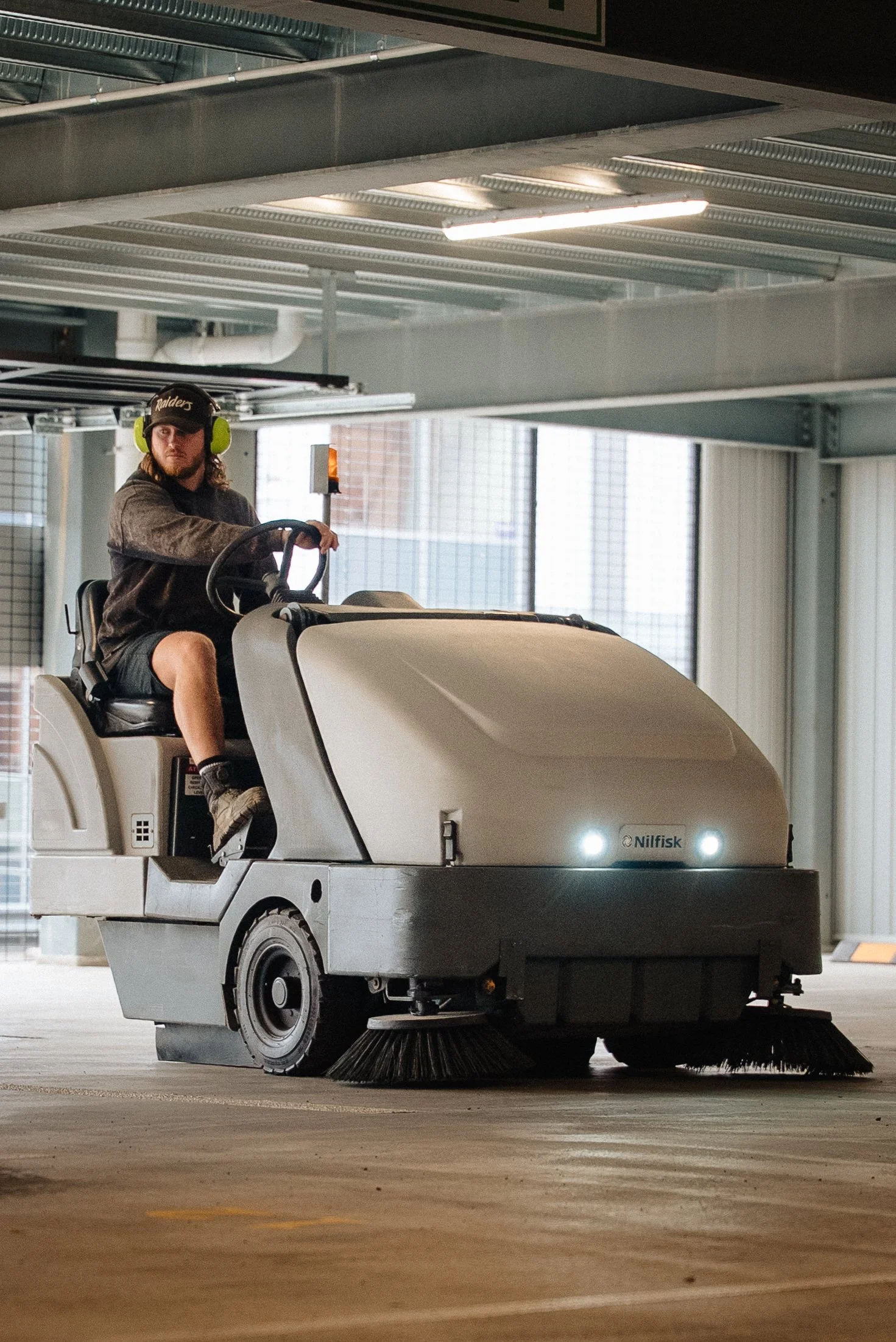 A person operating a floor cleaning machine in an indoor parking garage.
