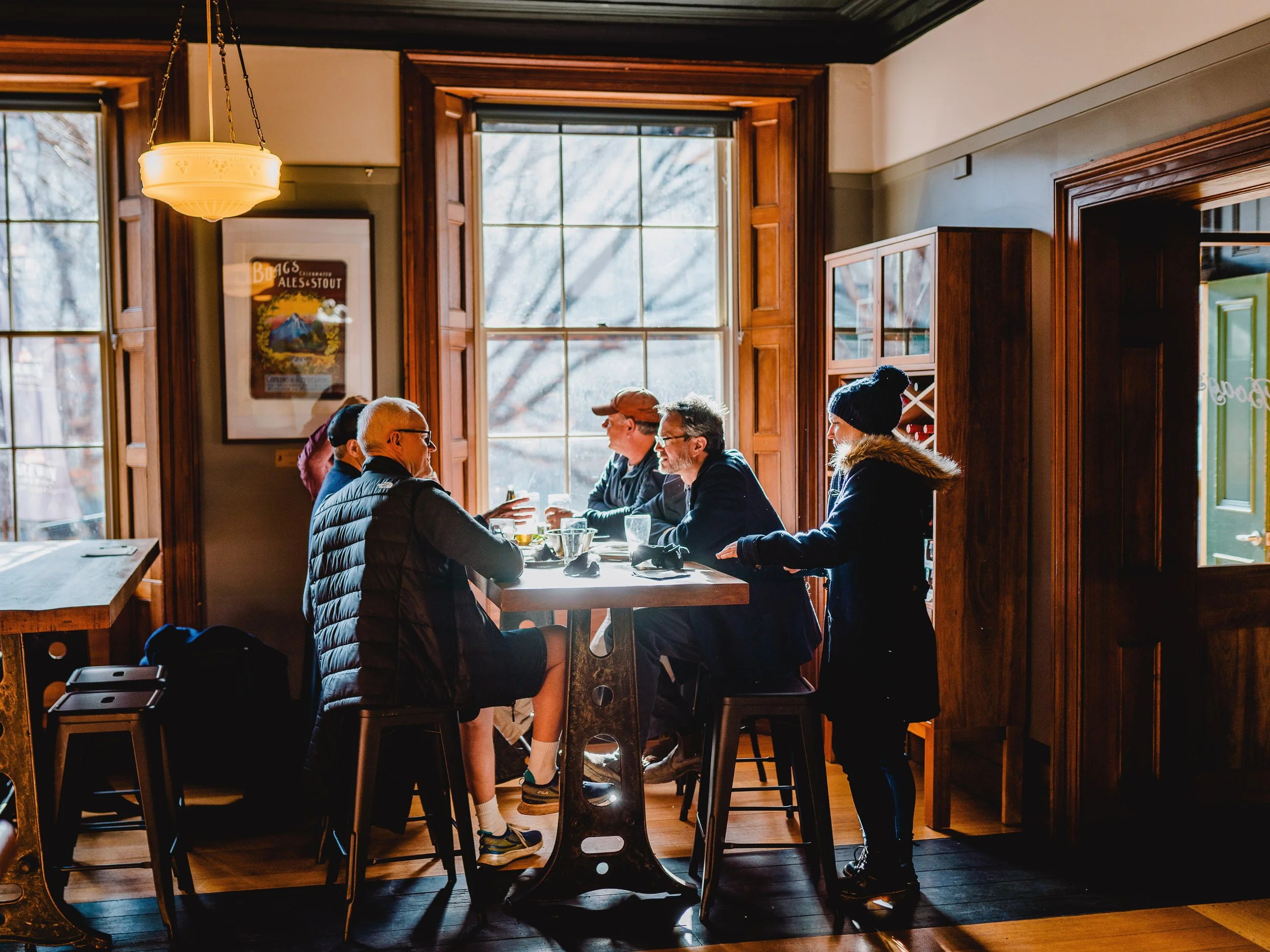 People sitting and talking at a high table in a cozy restaurant with large windows and wooden interior.